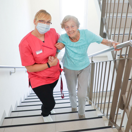 Eine Pflegekraft hilft einer älteren Dame beim Treppensteigen 