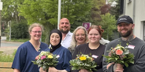 6 Personen stehen mit Blumensträußen vor einem Baum