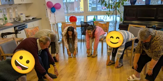 Bewohnerinnen und Bewohner strecken sich zum Boden, in der Mitte machen Diylan und Rojin die Übung vor
