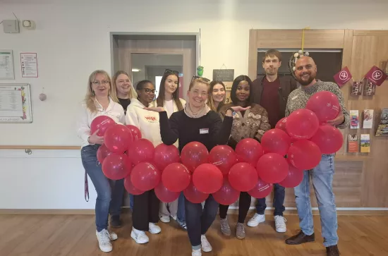Neun Menschen halten eine Luftballongirlande