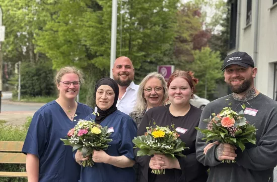 6 Personen stehen mit Blumensträußen vor einem Baum