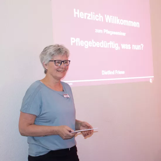 Frau steht vorne und hält eine Präsentation mit einer PPT im Hintergrund.